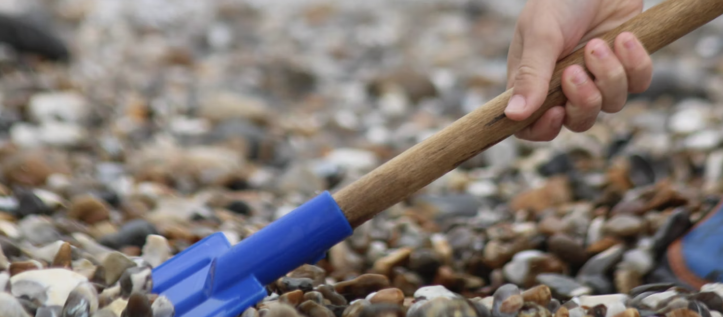 person digging a hole in gravel with a blue shovel